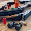 Shotgun shells beside a break-action shotgun and binoculars